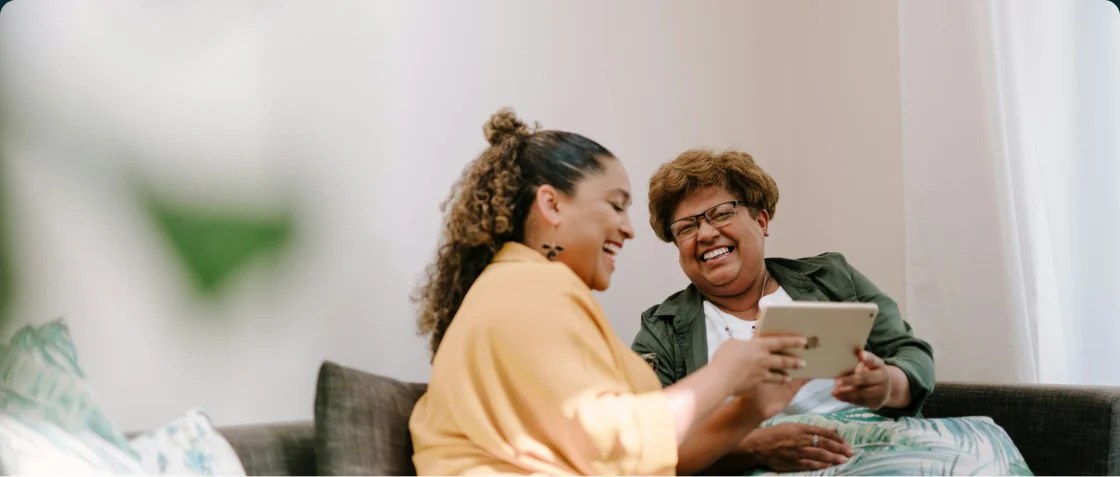 A caregiver and an older woman smiling at a tablet